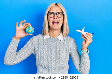 Beautiful Blonde Woman Holding Airplane Toy And World Ball Angry And Mad Screaming Frustrated And Furious, Shouting With Anger Looking Up. 