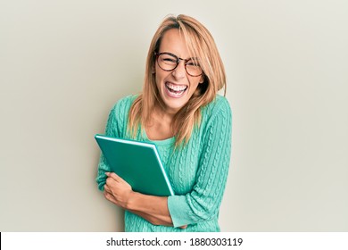 Beautiful Blonde Woman Holding Book Wearing Glasses Smiling And Laughing Hard Out Loud Because Funny Crazy Joke. 