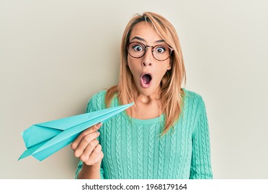 Beautiful Blonde Woman Holding Paper Airplane Scared And Amazed With Open Mouth For Surprise, Disbelief Face 