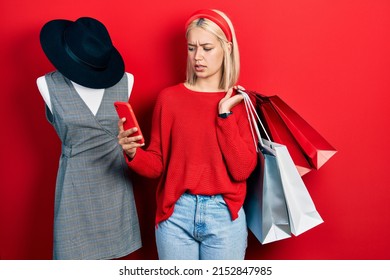 Beautiful Blonde Woman Holding Shopping Bags And Smartphone Clueless And Confused Expression. Doubt Concept. 