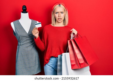 Beautiful Blonde Woman Holding Shopping Bags And Credit Card Clueless And Confused Expression. Doubt Concept. 