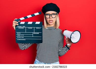 Beautiful Blonde Woman Holding Video Film Clapboard And Megaphone Clueless And Confused Expression. Doubt Concept. 