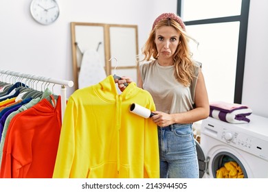 Beautiful blonde woman at laundry room cleaning clothes with pet hair remover roller depressed and worry for distress, crying angry and afraid. sad expression. 