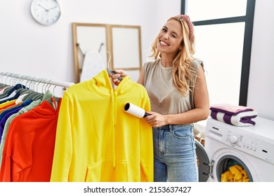 Beautiful blonde woman at laundry room cleaning clothes with pet hair remover roller winking looking at the camera with sexy expression, cheerful and happy face. 