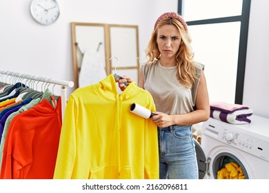 Beautiful blonde woman at laundry room cleaning clothes with pet hair remover roller skeptic and nervous, frowning upset because of problem. negative person. 