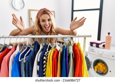 Beautiful blonde woman at laundry room with clean clothes celebrating crazy and amazed for success with open eyes screaming excited. 