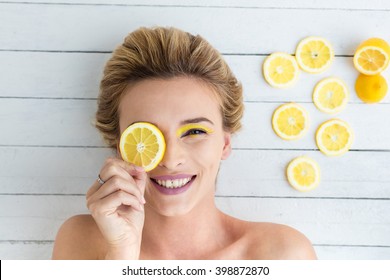 beautiful blonde woman laying on a white wooden background next to slices of lemon, having a slice of lemon on the eyes and smiling
 - Powered by Shutterstock