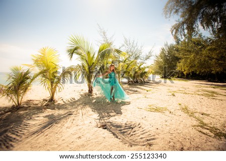 beautiful blonde woman pose in elegant dress in green palm leafs