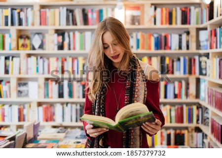 Beautiful blonde woman reading a book in a bookstore.