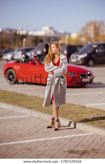 Beautiful blonde woman in a red dress posing in
a red car in the city on a sunny
day