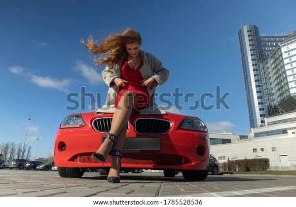 Beautiful blonde woman in a red dress posing in\
a red car in the city on a sunny\
day