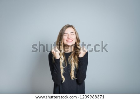 beautiful blonde woman rejoices with success with fists, isolated over black background