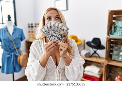 Beautiful blonde woman at retail boutique holding dollars banknotes angry and mad screaming frustrated and furious, shouting with anger looking up. 