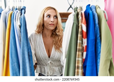 Beautiful Blonde Woman Searching Clothes On Clothing Rack Smiling Looking To The Side And Staring Away Thinking. 