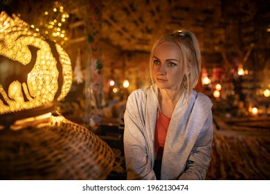 Beautiful Blonde Woman Sitting In The Old American Hippie Hut In Front Of The Lantern In The Evening - Low Light Portrait.