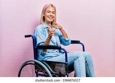 Beautiful blonde woman sitting on wheelchair pointing fingers to camera with happy and funny face. good energy and vibes.  - Powered by Shutterstock