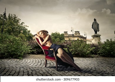 Beautiful blonde woman sitting in a red chair in the middle of a square