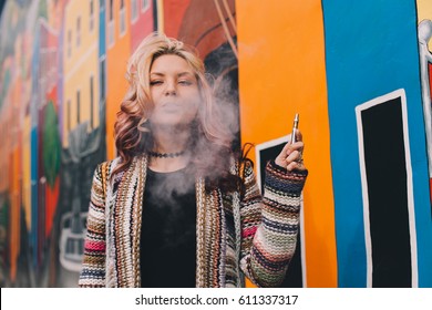 Beautiful Blonde Woman Smoking a Cannabis Vape Pen Against a Colorful Mural