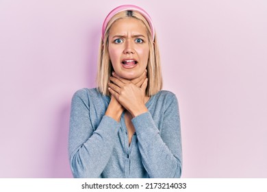 Beautiful blonde woman standing over pink background shouting and suffocate because painful strangle. health problem. asphyxiate and suicide concept. 
