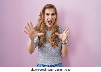 Beautiful Blonde Woman Standing Over Pink Background Afraid And Terrified With Fear Expression Stop Gesture With Hands, Shouting In Shock. Panic Concept. 