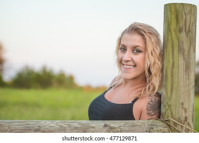 Beautiful Blonde Woman With Tattoo Leaning On Fence Post