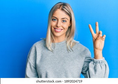 Beautiful blonde woman wearing casual clothes showing and pointing up with fingers number two while smiling confident and happy. 