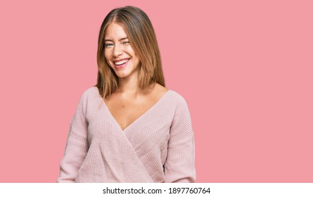 Beautiful blonde woman wearing casual winter pink sweater winking looking at the camera with sexy expression, cheerful and happy face. 