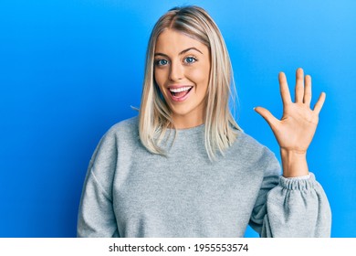 Beautiful blonde woman wearing casual clothes showing and pointing up with fingers number five while smiling confident and happy. 