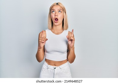 Beautiful Blonde Woman Wearing Casual Style With Sleeveless Shirt Amazed And Surprised Looking Up And Pointing With Fingers And Raised Arms. 