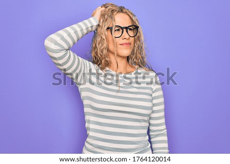 Beautiful blonde woman wearing casual striped t-shirt and glasses over purple background confuse and wondering about question. Uncertain with doubt, thinking with hand on head. Pensive concept.