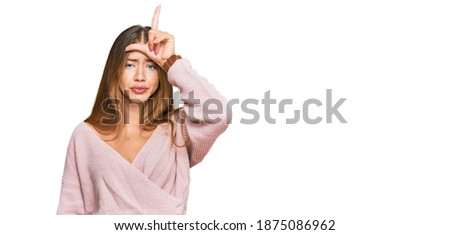 Beautiful blonde woman wearing casual winter pink sweater making fun of people with fingers on forehead doing loser gesture mocking and insulting. 