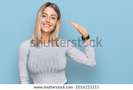 Beautiful blonde woman wearing casual clothes waiving saying hello happy and smiling, friendly welcome gesture 