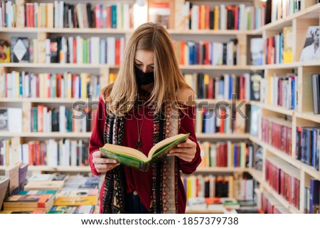 Beautiful blonde woman wearing a face mask with a book in a bookstore.