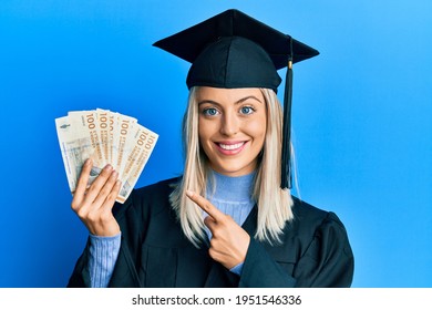 Beautiful Blonde Woman Wearing Graduation Cap And Ceremony Robe Holding Denmark Krone Smiling Happy Pointing With Hand And Finger 