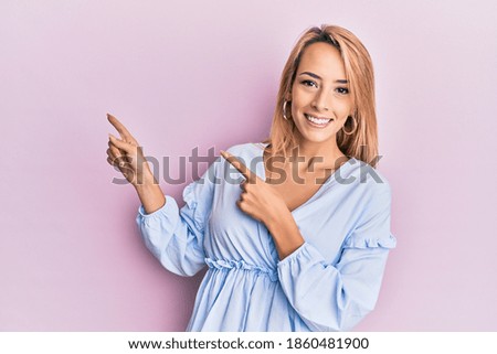 Beautiful blonde woman wearing summer dress smiling and looking at the camera pointing with two hands and fingers to the side. 