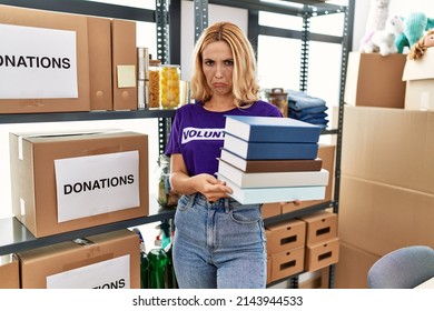 Beautiful blonde woman wearing volunteer t shirt holding books depressed and worry for distress, crying angry and afraid. sad expression. 