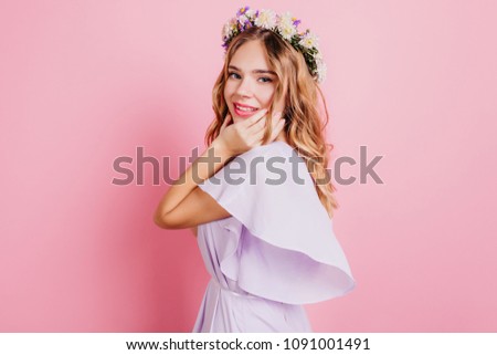 Beautiful blonde woman wears stylish wreath posing in studio with pink interior. Portrait of gorgeous caucasian girl with floral accessory.