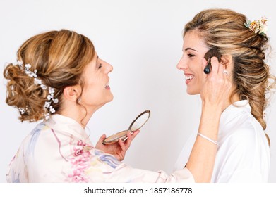 Beautiful blonde woman in white dress on her wedding day before getting married, her mother does her makeup. - Powered by Shutterstock