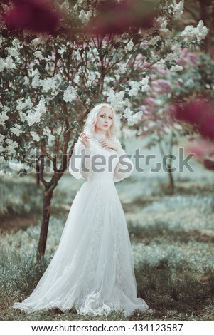 Beautiful blonde woman in white vintage dress in blooming garden. 