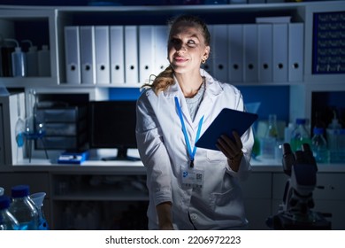 Beautiful Blonde Woman Working At Scientist Laboratory Late At Night Smiling Looking To The Side And Staring Away Thinking. 