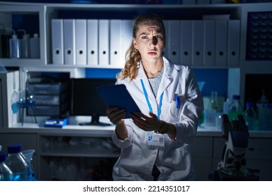 Beautiful Blonde Woman Working At Scientist Laboratory Late At Night In Shock Face, Looking Skeptical And Sarcastic, Surprised With Open Mouth 