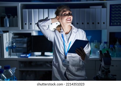 Beautiful Blonde Woman Working At Scientist Laboratory Late At Night Smiling Confident Touching Hair With Hand Up Gesture, Posing Attractive And Fashionable 