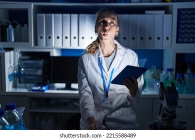 Beautiful Blonde Woman Working At Scientist Laboratory Late At Night Making Fish Face With Lips, Crazy And Comical Gesture. Funny Expression. 