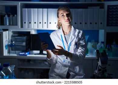 Beautiful Blonde Woman Working At Scientist Laboratory Late At Night Relaxed With Serious Expression On Face. Simple And Natural Looking At The Camera. 