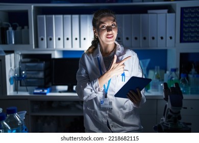 Beautiful Blonde Woman Working At Scientist Laboratory Late At Night Cheerful With A Smile On Face Pointing With Hand And Finger Up To The Side With Happy And Natural Expression 