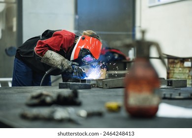 Beautiful blonde woman works as a welder in workshop, operating welding machine, wearing protective clothing and a welding mask. - Powered by Shutterstock