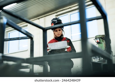 Beautiful blonde woman works as a welder in workshop, reading blueprints, wearing protective clothing and a welding mask. - Powered by Shutterstock