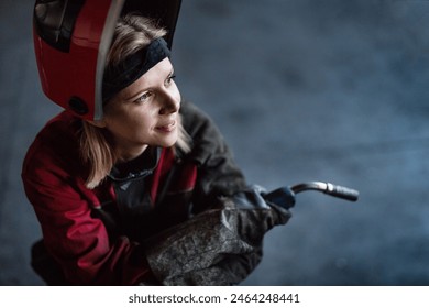 Beautiful blonde woman works as a welder in workshop, operating welding machine, wearing protective clothing and a welding mask. - Powered by Shutterstock