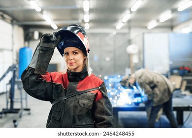 Beautiful blonde woman works as a welder in workshop, operating welding machine, wearing protective clothing and a welding mask. - Powered by Shutterstock