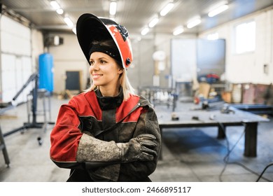 Beautiful blonde woman works as a welder in workshop, operating welding machine, wearing protective clothing and a welding mask. - Powered by Shutterstock